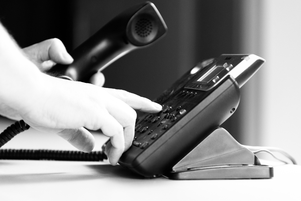 black and white photo of a person's hands diialing an office style touch tone phone while holding the receiver